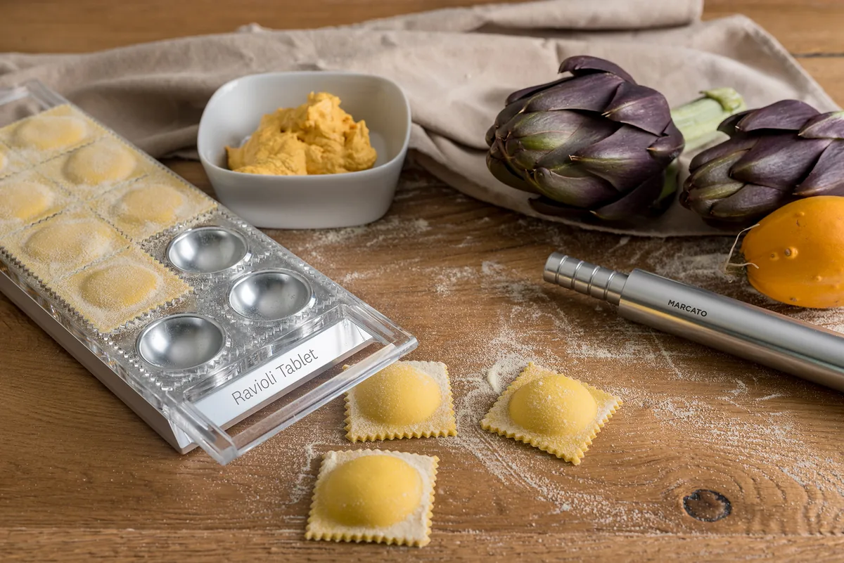 Tableta de raviolis con las piezas ya formadas junto al cuenco de relleno